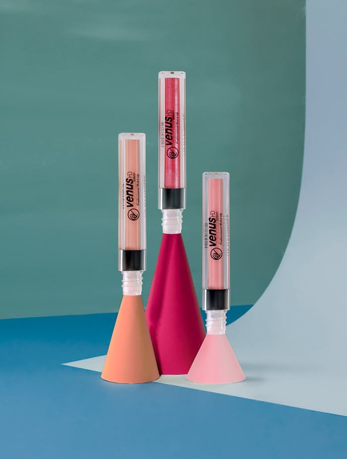 Stylish lip gloss tubes displayed on modern geometric shapes, perfect for beauty and fashion themes.
